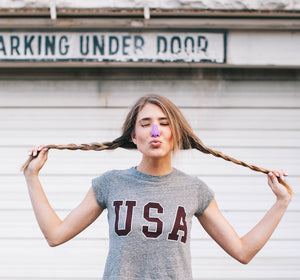 Woman holding braids up and making a pout face while wearing purple SPF by Nöz on nose